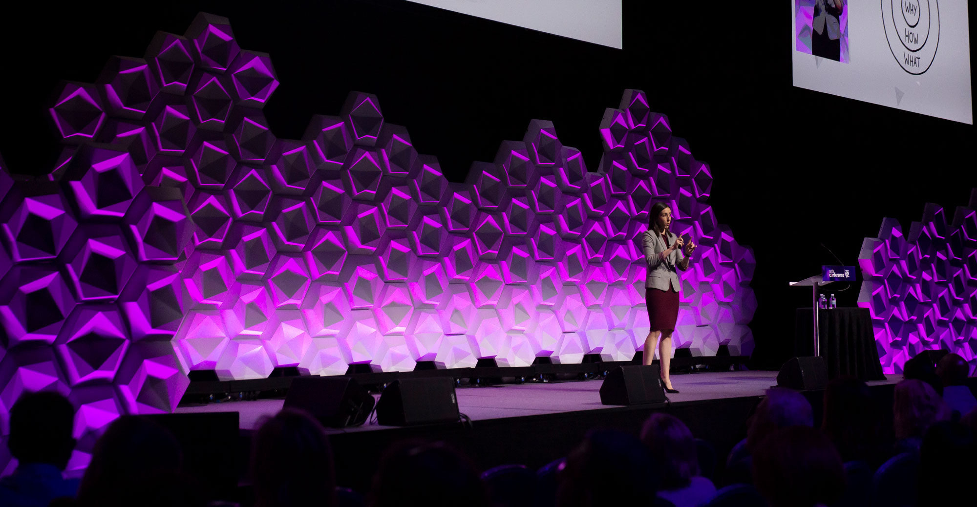 Holly Ransom speaking on stage against a purple geometric backdrop