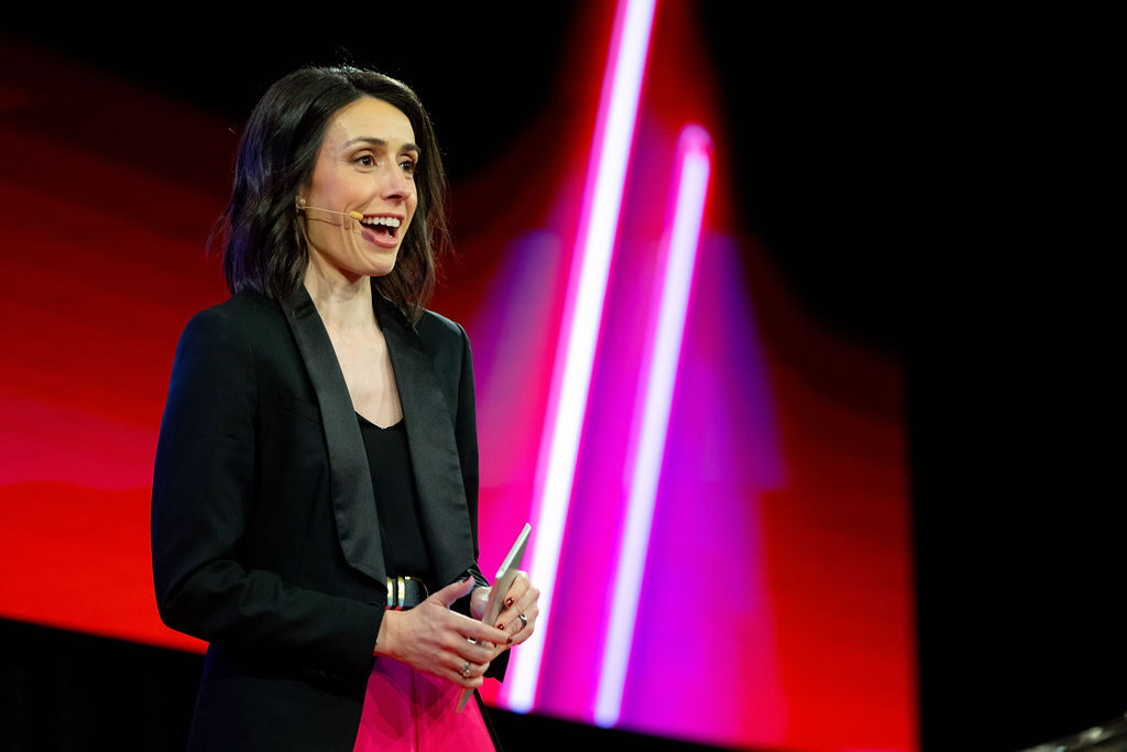 Holly Ransom in black jacket delivering keynote on stage